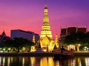 Golden Buddhist temple and illuminated pagoda at sunset in Bangkok, Thailand, showcasing the best time to visit Bangkok with vibrant purple skies and traditional Thai architecture.